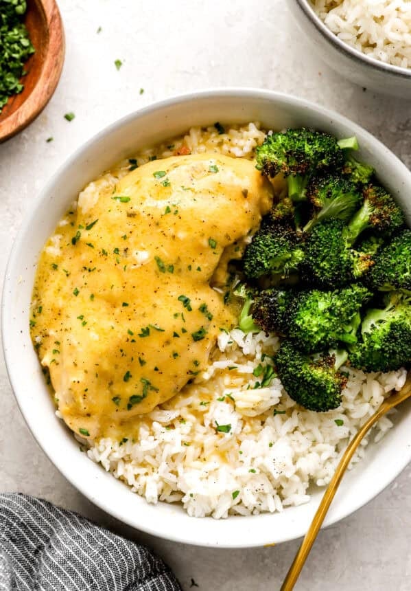 a serving of crockpot ranch chicken in a white bowl with rice and broccoli.