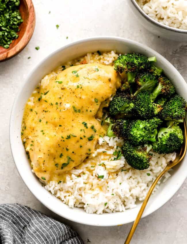 a serving of crockpot ranch chicken in a white bowl with rice and broccoli.