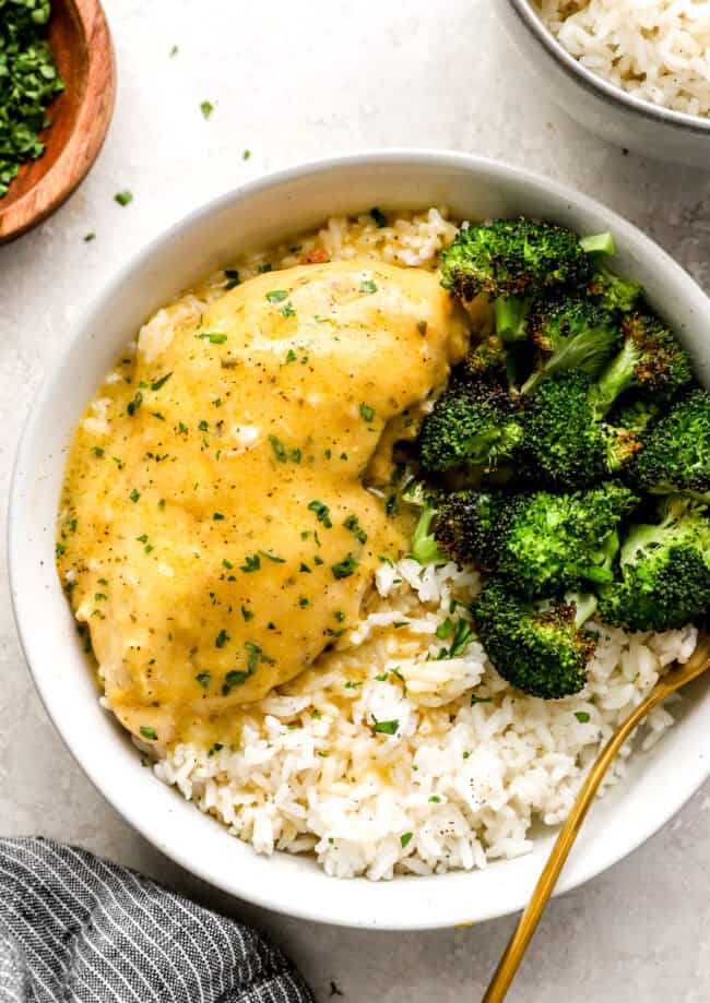 a serving of crockpot ranch chicken in a white bowl with rice and broccoli.