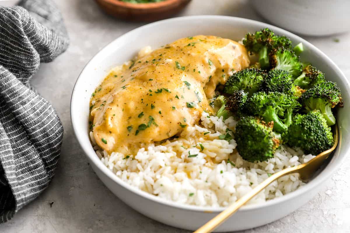 a serving of crockpot ranch chicken in a white bowl with rice and broccoli.