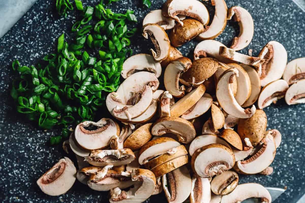 Chopped mushrooms and green onions on a cutting board.