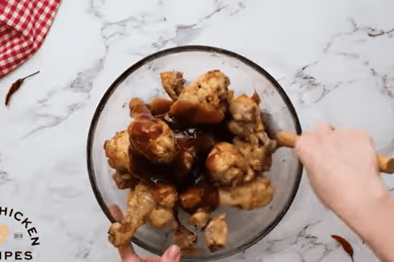 Instant Pot chicken drumsticks in a glass bowl being tossed with bbq sauce.