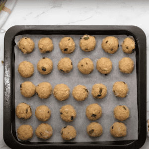 Uncooked ground chicken meatballs lined up on a baking sheet lined with parchment paper.