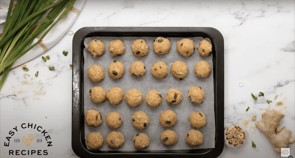 Uncooked ground chicken meatballs lined up on a baking sheet lined with parchment paper.