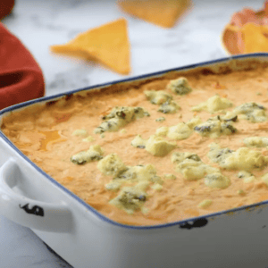 A white baking dish filled with buffalo chicken dip topped with blue cheese crumbles.