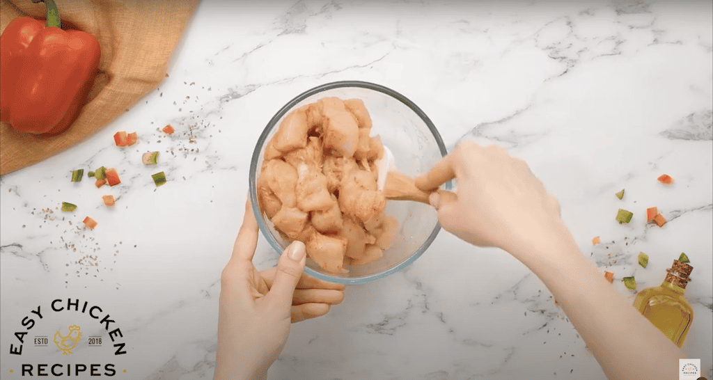 Combining cubes of raw chicken with spices in a glass mixing bowl.