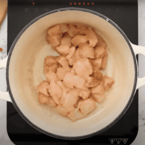 Cubes of chicken cooking in a large pot.