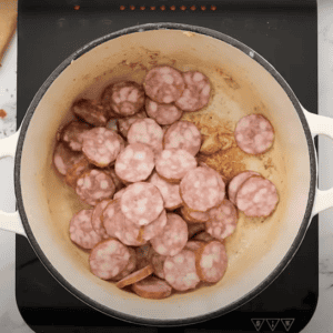 Slices of sausage cooking in a large pot.