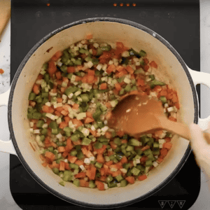 Sauteing diced onion, celery, and bell peppers in a large pot.