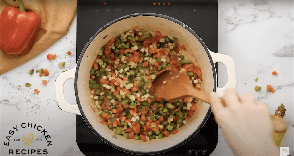 Sauteing diced onion, celery, and bell peppers in a large pot.