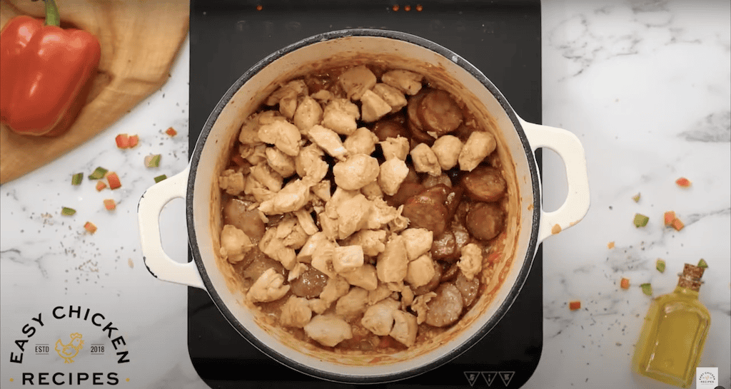 Cubes of chicken and sausage added to a pot of jambalaya.