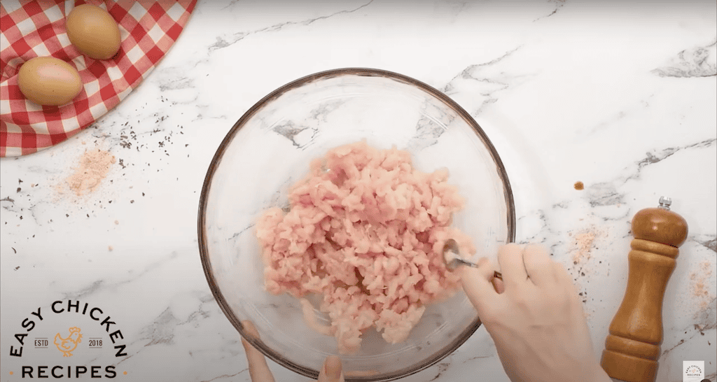 Crumbling raw ground chicken in a glass mixing bowl.