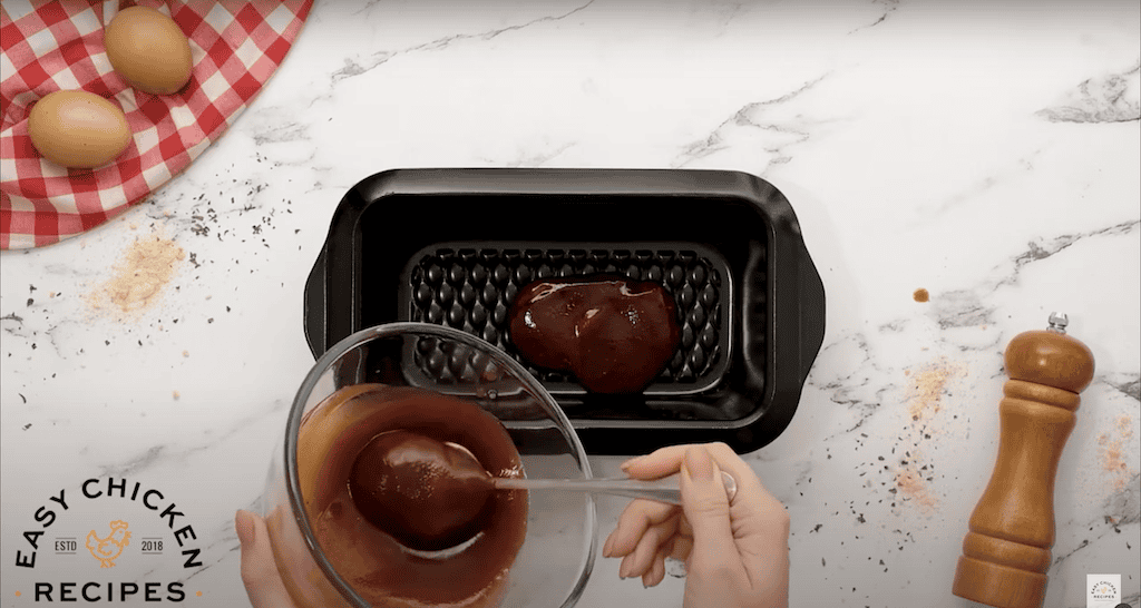 Spreading ketchup glaze into the bottom of a loaf pan.