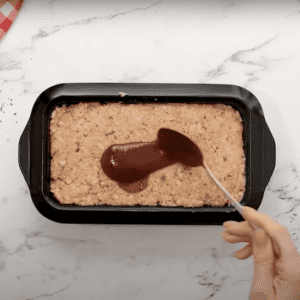 Spreading ketchup glaze on top of a chicken meatloaf.