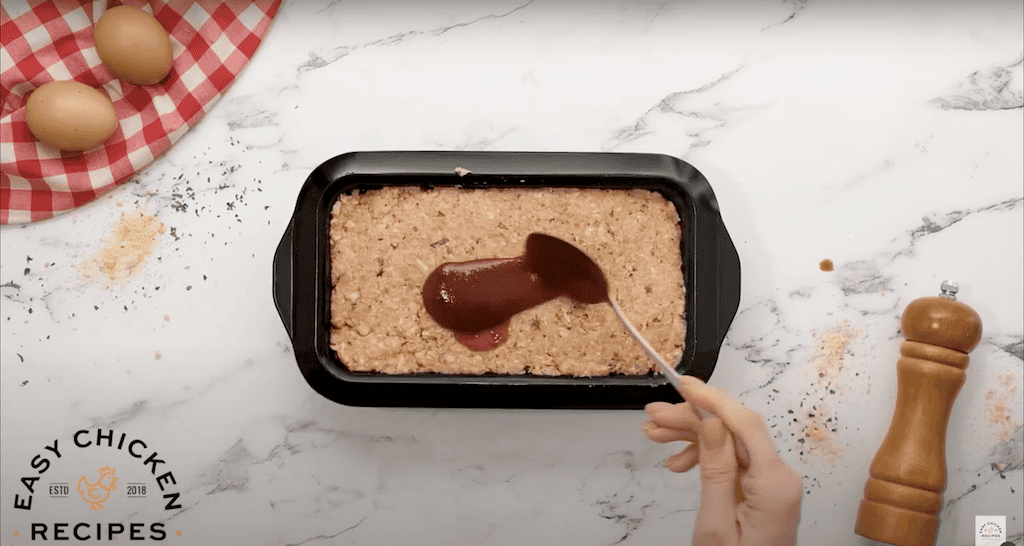 Spreading ketchup glaze on top of a chicken meatloaf.