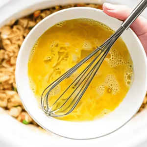 scrambled raw egg in a bowl with a whisk.