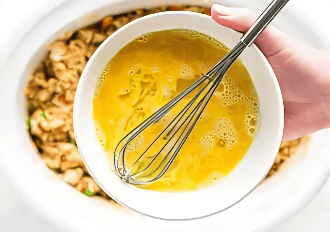 scrambled raw egg in a bowl with a whisk.