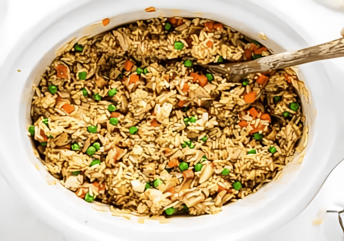 chicken fried rice in a crockpot with a wooden spoon.