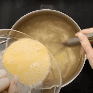 Pouring beaten eggs into a pot of chicken broth, while stirring.