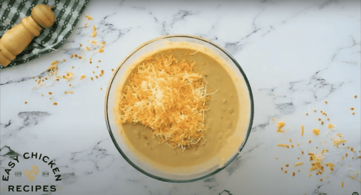 Shredded cheese placed on top of a casserole mixture, in a mixing bowl.