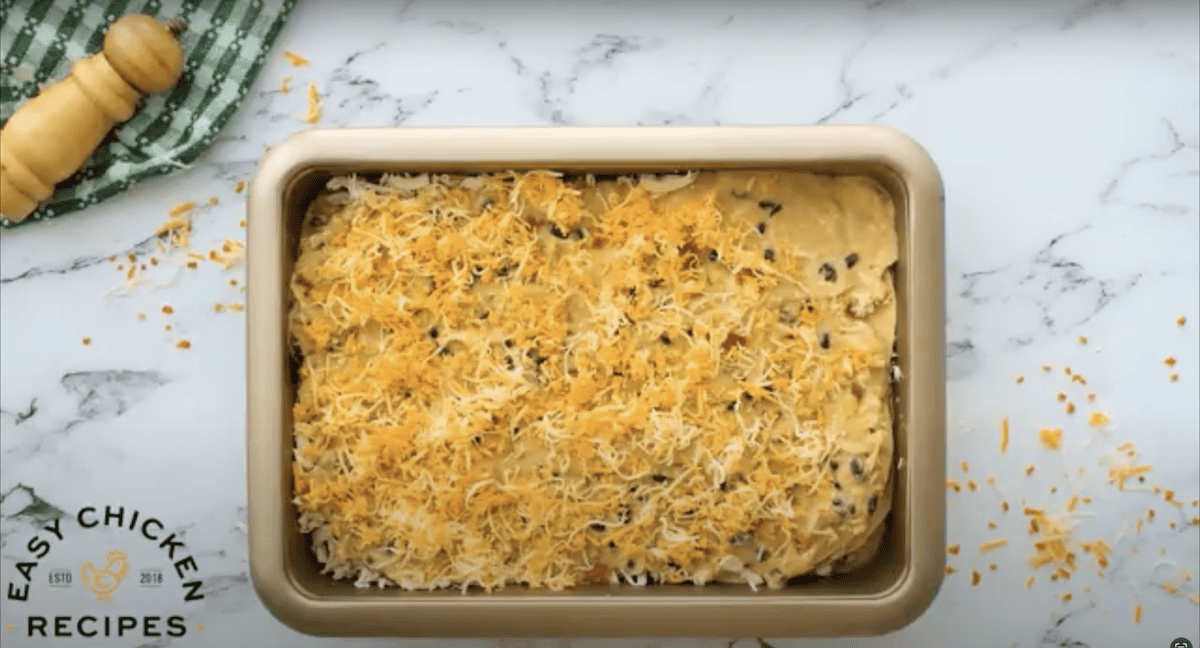 Unbaked casserole topped with shredded cheese.