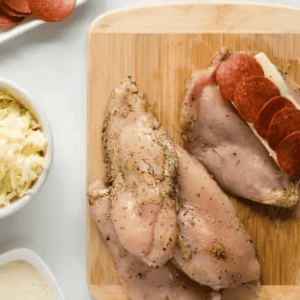 stuffing chicken breasts with cheese and pepperoni on a cutting board.