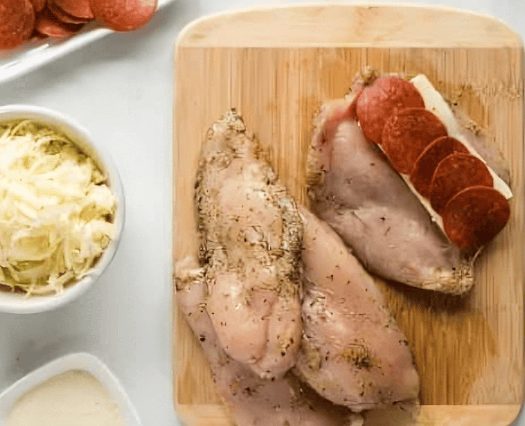 stuffing chicken breasts with cheese and pepperoni on a cutting board.