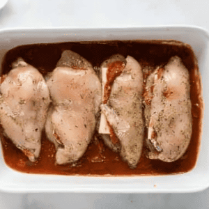 cheese and pepperoni stuffed chicken breasts on a bed of sauce in a baking pan.