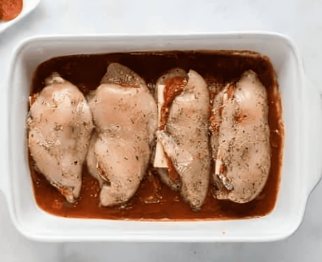 cheese and pepperoni stuffed chicken breasts on a bed of sauce in a baking pan.