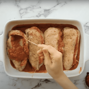 Spreading marinara on top of 4 stuffed chicken breasts in a baking dish.