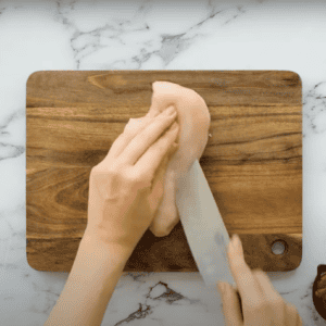 Hand slicing into the side of a chicken breast with a Chef's knife.