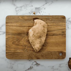 A chicken breast coated in spices, on a cutting board.