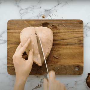 Hands opening a sliced chicken breast to butterfly it.