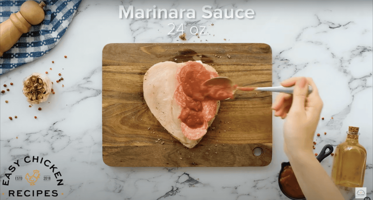Smoothing marinara sauce on top of the chicken.