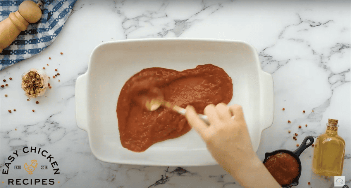 Spreading marinara sauce into the bottom of a baking dish.