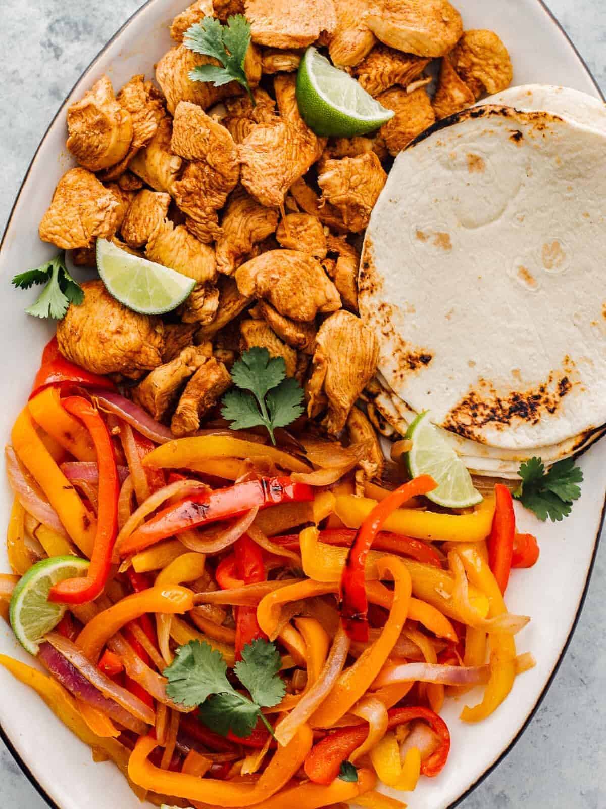 A platter of instant pot chicken fajitas filling with tortillas and lime wedges.