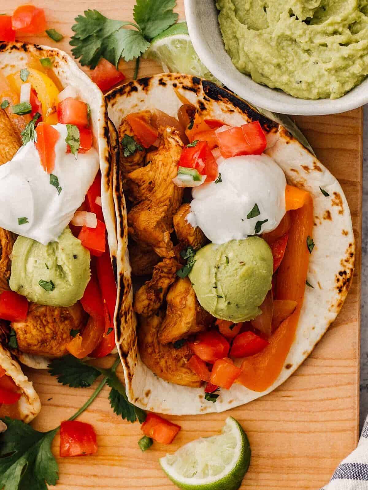 Close up on chicken fajitas on a cutting board, topped with guacamole and sour cream.