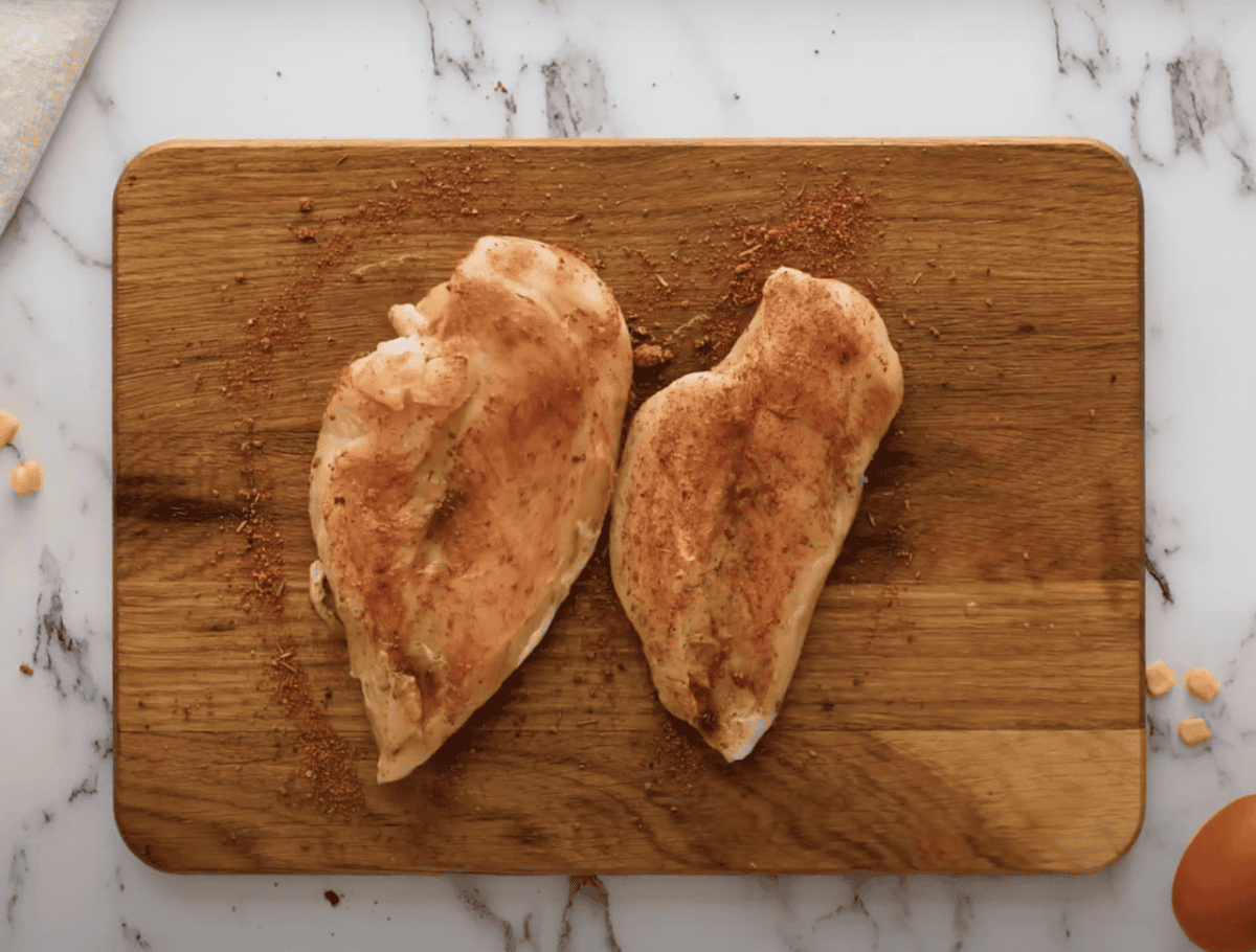 Two uncooked chicken breasts covered in a barbecue rub.