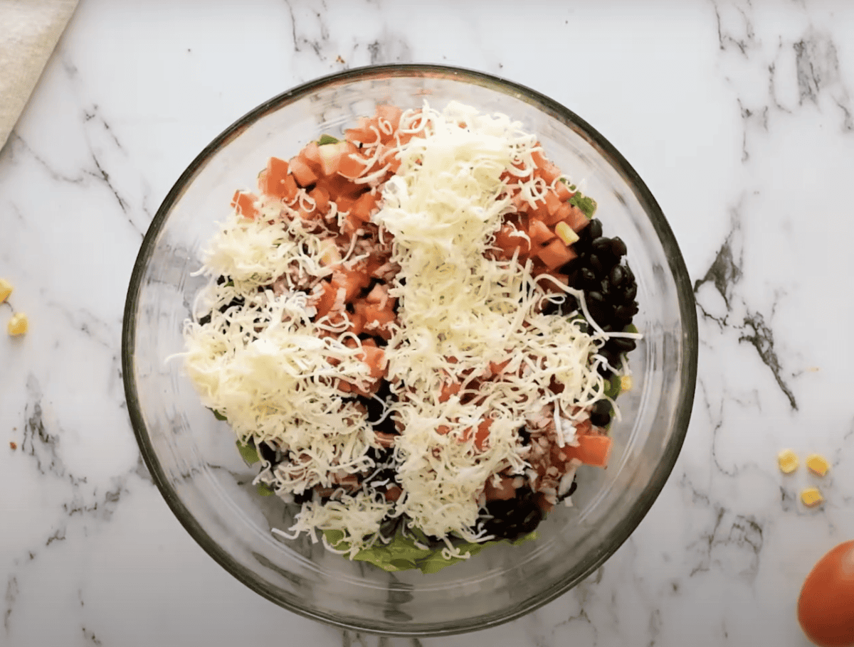 Lettuce, black beans, corn, tomatoes, and cheese combined in a glass bowl.