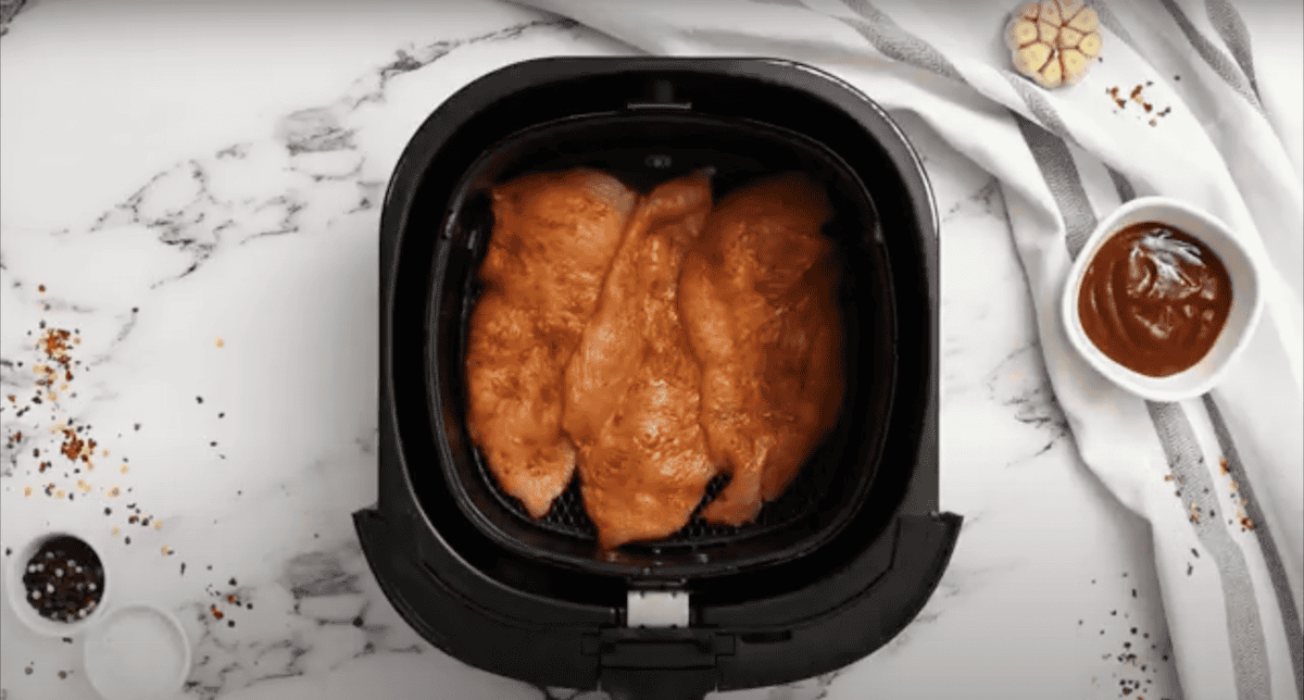 3 seasoned chicken breasts in the basket of an Air Fryer.