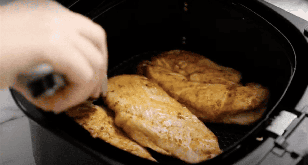 Flipping chicken breasts in an Air Fryer basket.