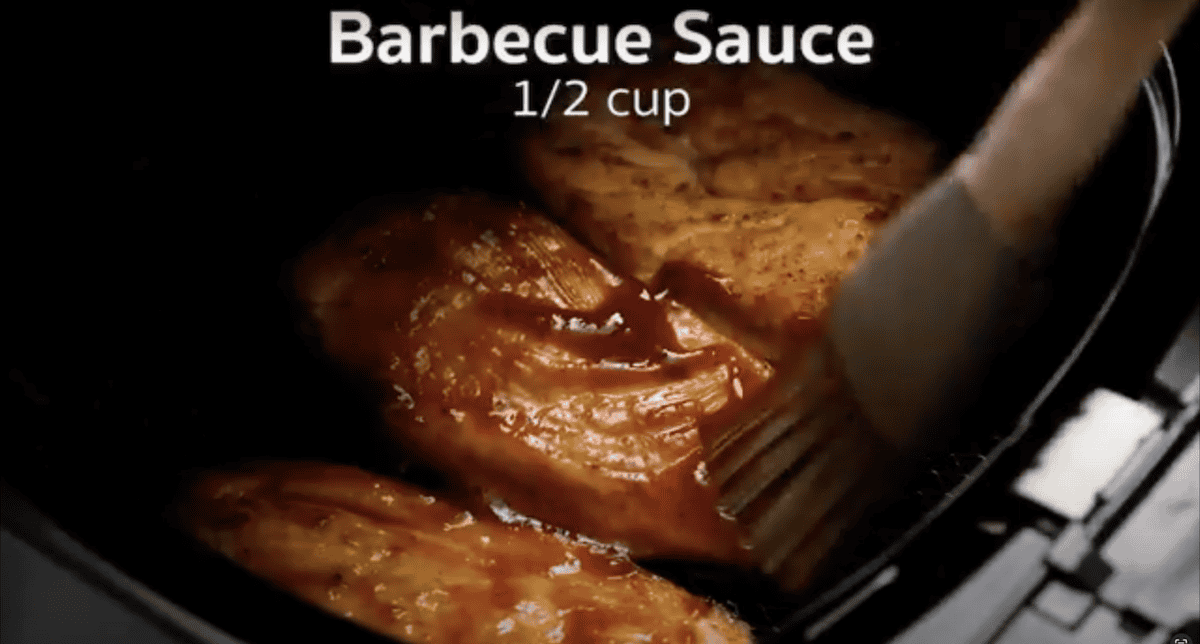 Brushing barbecue sauce onto chicken breasts in an Air Fryer.