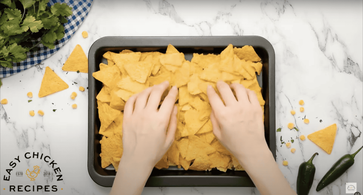 Hands spreading tortilla chips onto a baking tray.