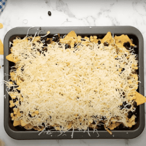 Baking tray filled with tortilla chips and shredded cheese.