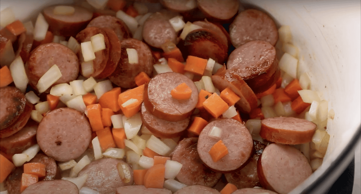 Sausage, onion, and carrots cooking in a Dutch oven.