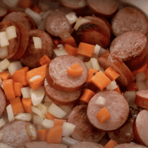 Sausage, onion, and carrots cooking in a Dutch oven.