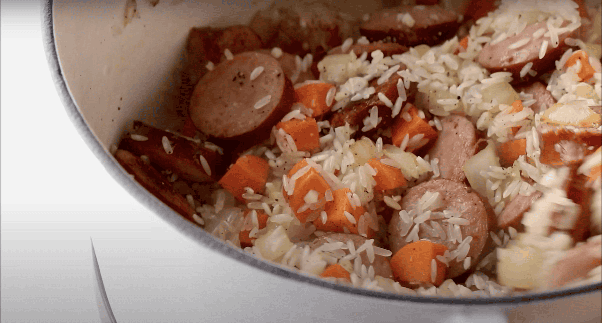 Sausage, carrots, onion, and rice cooking in a pot.