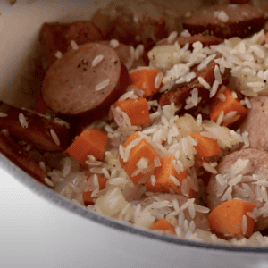 Sausage, carrots, onion, and rice cooking in a pot.