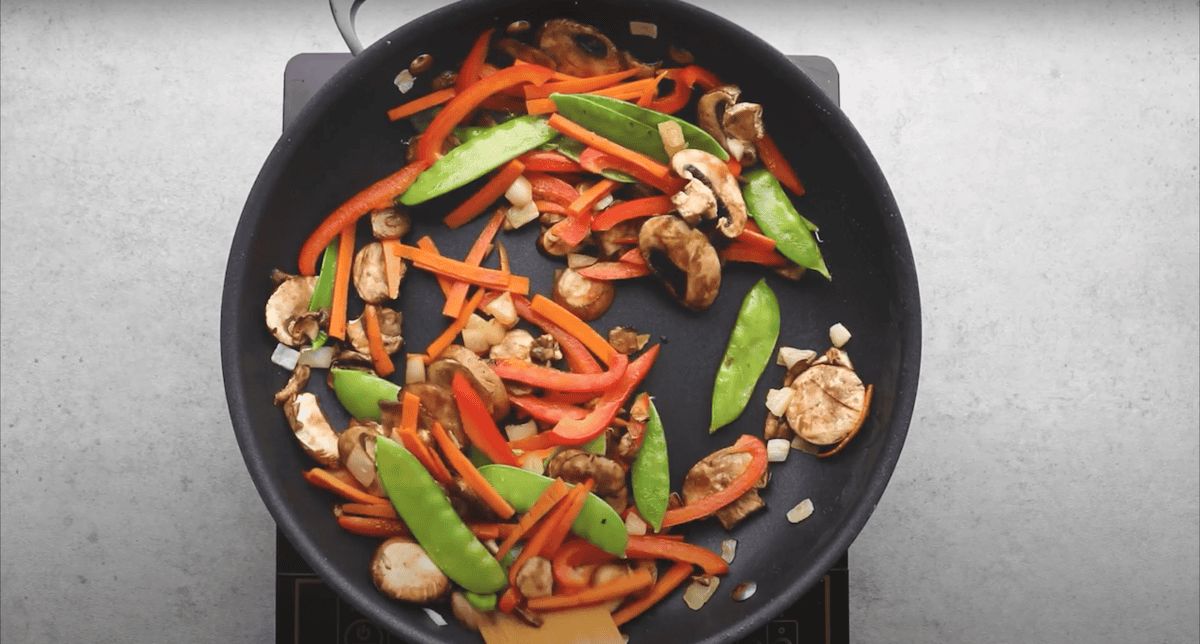 Carrots, red bell peppers, snow peas, and mushrooms cooking in a pan.