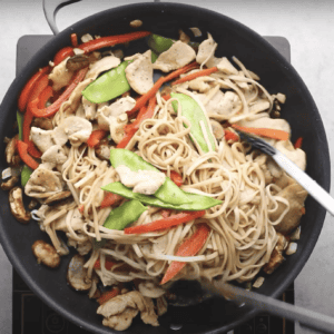 Cooking chicken lo mein in a skillet.